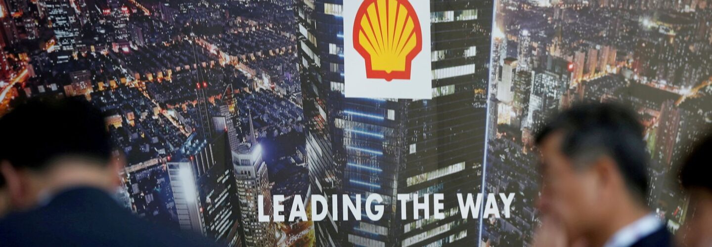 two men in suits with a Shell Oil logo behind them and an aerial view of a city