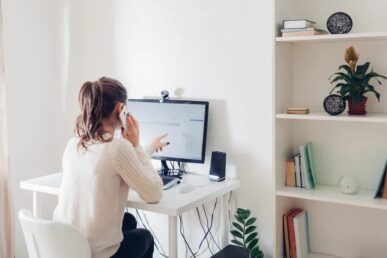 Woman talking on phone at desk in home office with computer